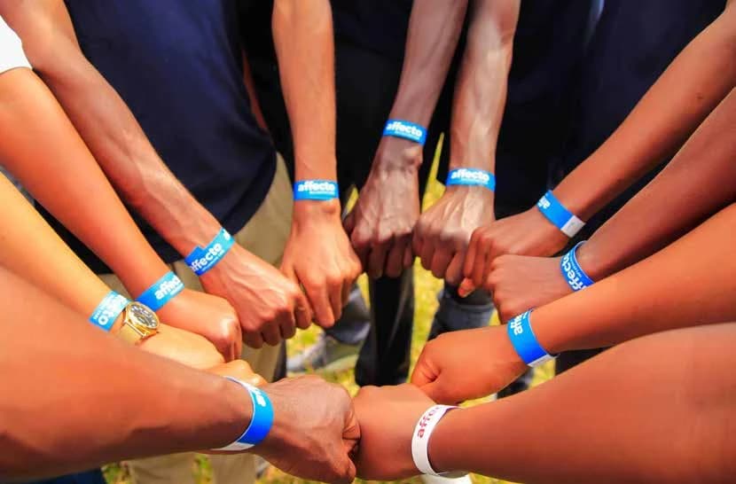 A circle of hands wearing colourful bracelets, coming together as a community